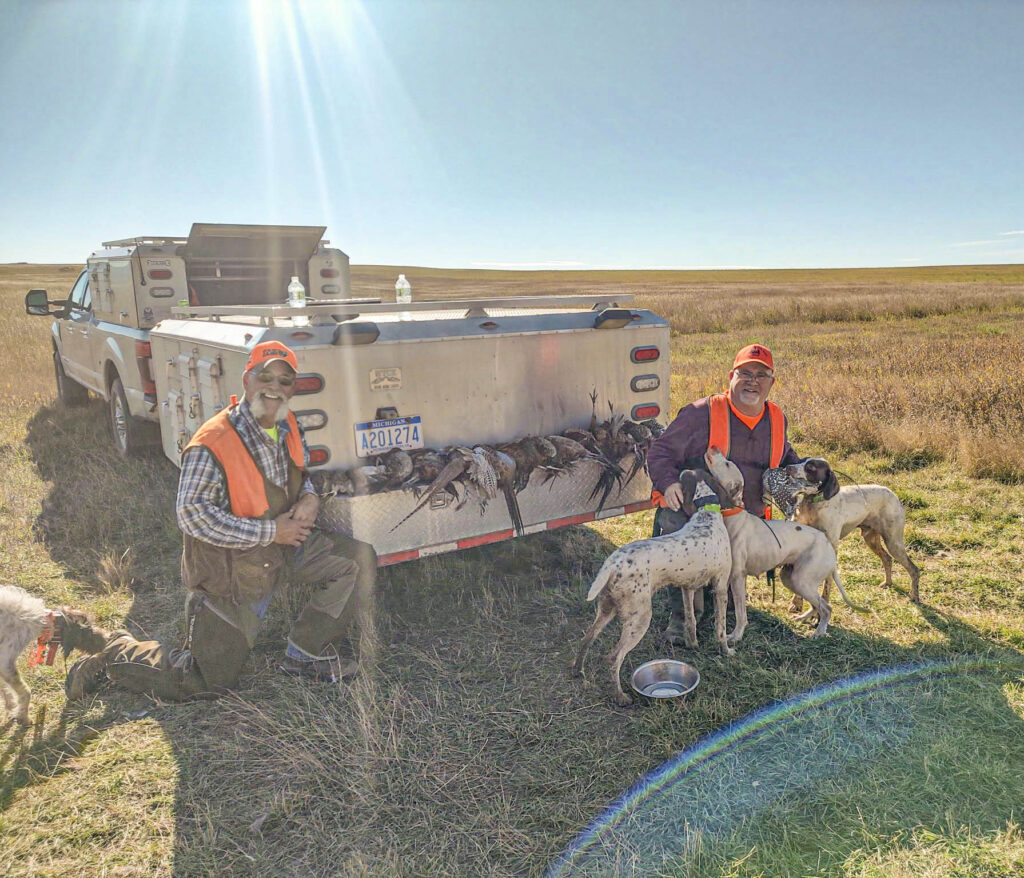 Two upland bird hunters with their dogs in the western prairie after a hunt.