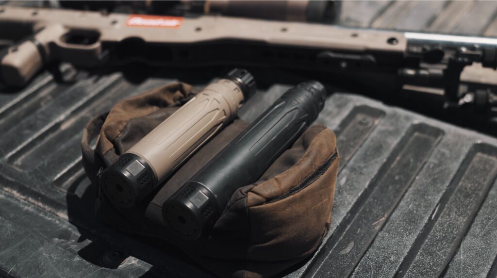 A rifle and two silencers on a truck tailgate.