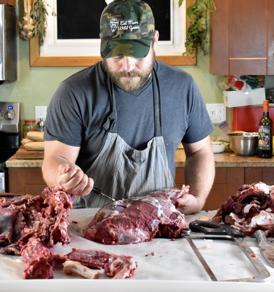 A hunter with a knife butchering deer venison in a kitchen.
