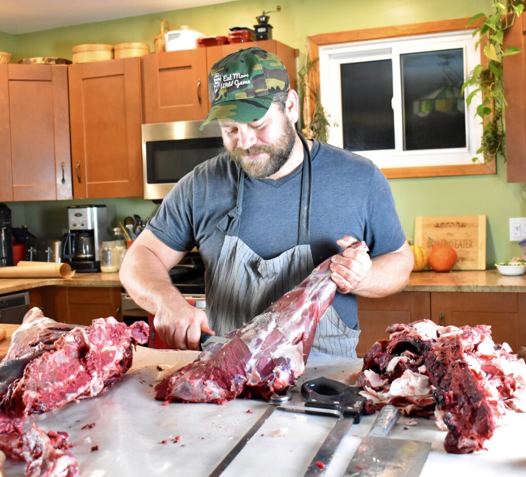A hunter cutting up deer venison in a kitchen.