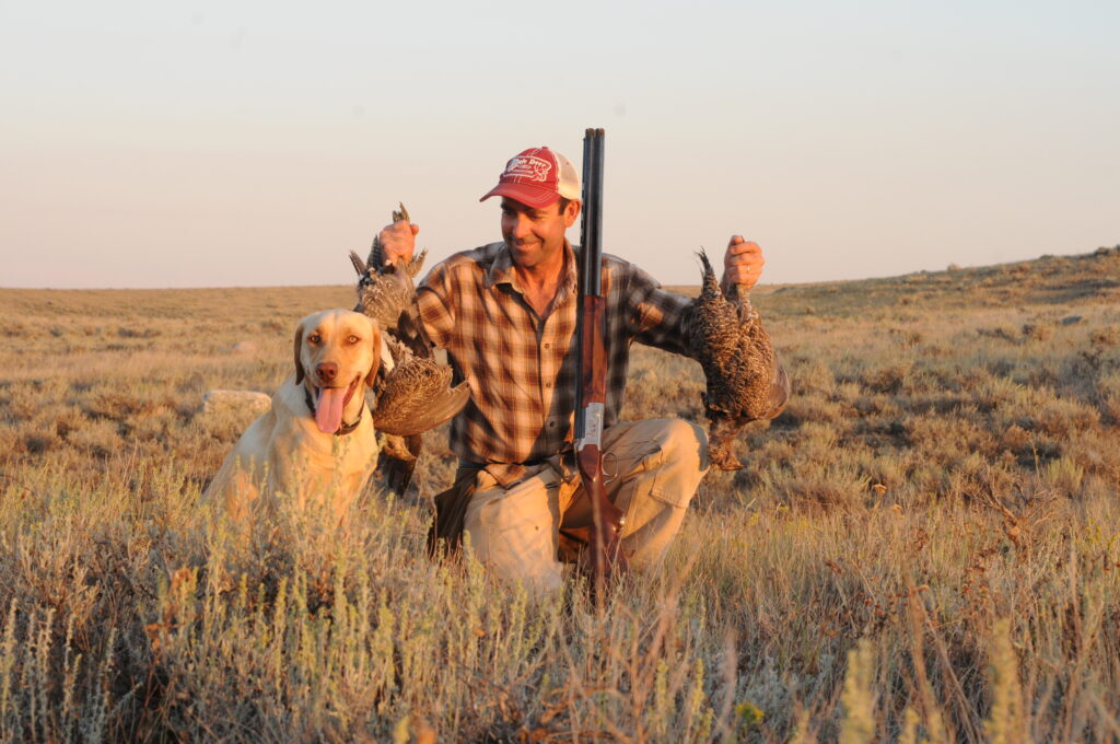 An upland bird hunter in a Montana prairie with a limit of sharp-tailed grouse and a yellow Labrador.