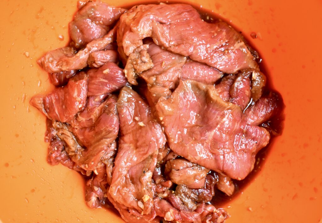 Meat marinating in a bowl with marinade for making jerky.