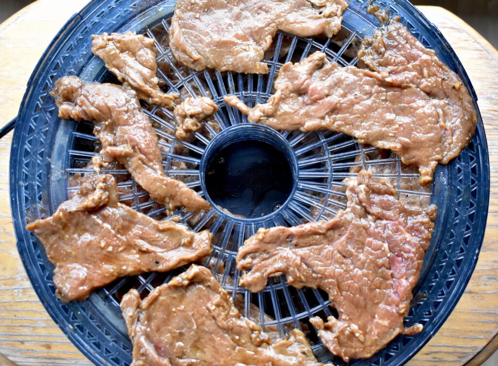 A food dehydrator tray with marinated meat ready for dehydrating to make jerky.