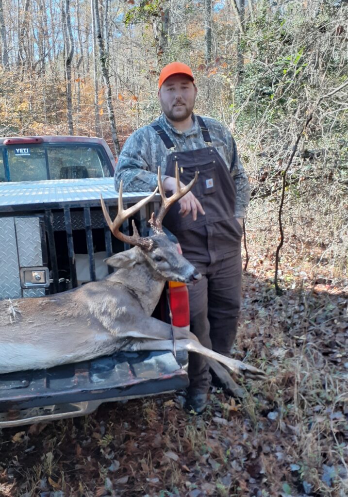 A hunter with a huge white-tailed buck on the tailgate of a pickup truck.
