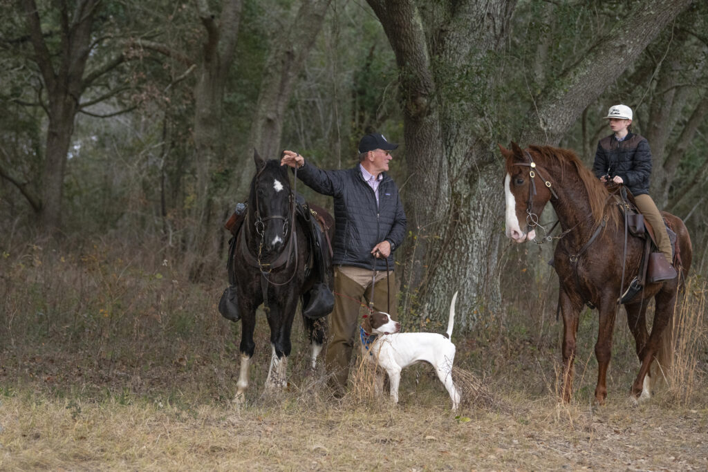 A man and a boy on a horse during a pointing dog field trial in the southern pines.