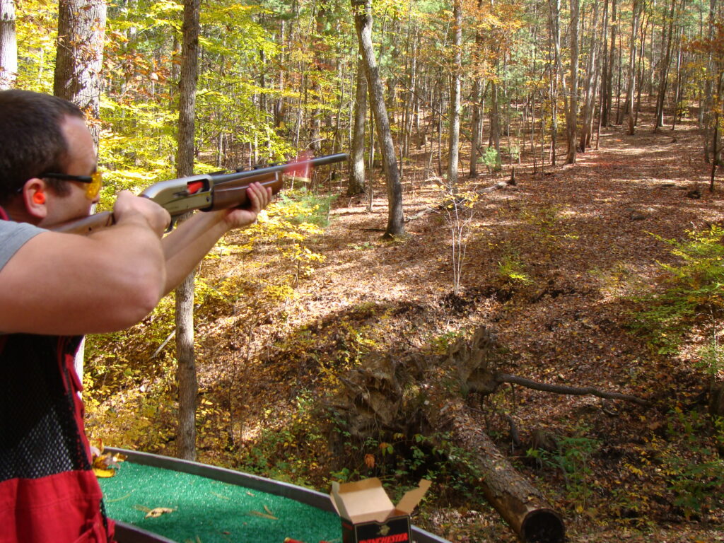 A sporting clays shooting in the woods looking down the barrel of a shotgun.