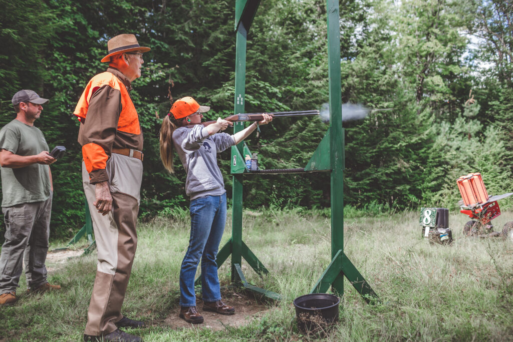 A youth shooter with an instructor on a trap range shooting clay targets.