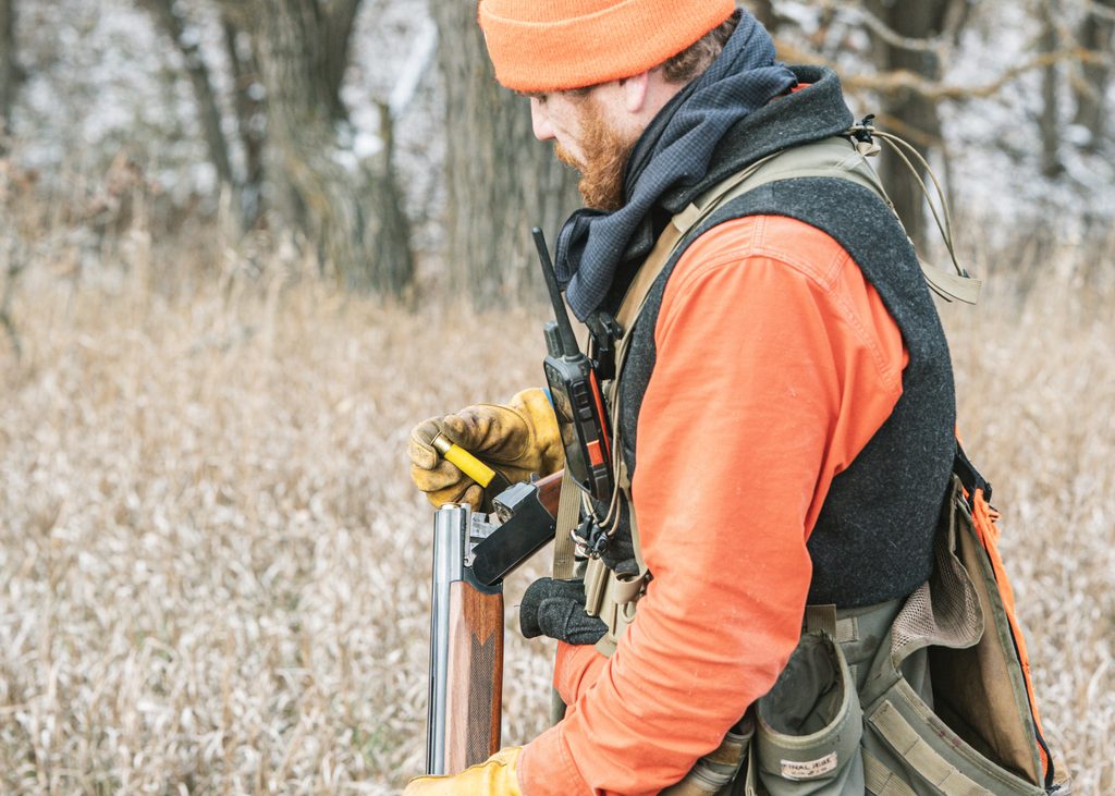 A hunter loading a shotshell into his shotgun.